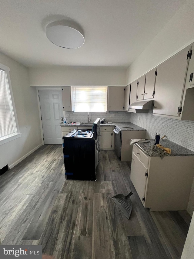 kitchen with dark wood-type flooring, dark stone countertops, decorative backsplash, and sink