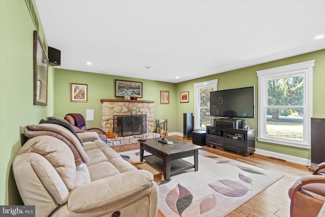 living room with a stone fireplace and light hardwood / wood-style flooring