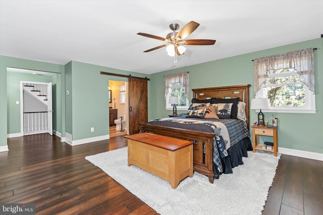 bedroom featuring multiple windows, ceiling fan, a barn door, ensuite bathroom, and dark wood-type flooring