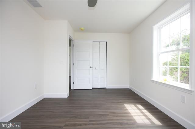 unfurnished bedroom with dark wood-type flooring, a closet, and multiple windows