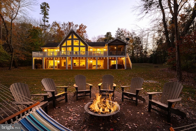 back house at dusk with a wooden deck, a lawn, and a fire pit