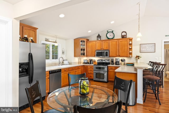 kitchen with lofted ceiling, a kitchen breakfast bar, light hardwood / wood-style flooring, decorative light fixtures, and appliances with stainless steel finishes