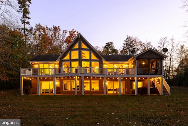 back house at dusk featuring a wooden deck and a lawn