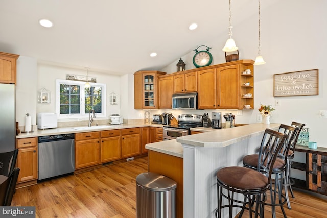 kitchen with kitchen peninsula, a breakfast bar area, appliances with stainless steel finishes, light hardwood / wood-style flooring, and sink