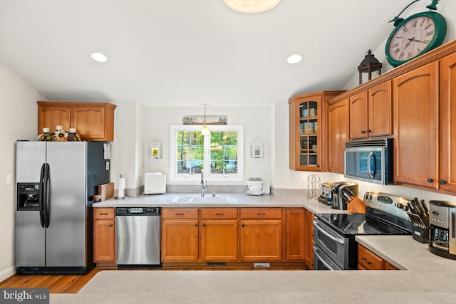 kitchen with vaulted ceiling, stainless steel appliances, sink, and light wood-type flooring