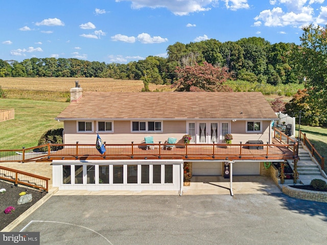 back of property with a wooden deck, a rural view, and a garage