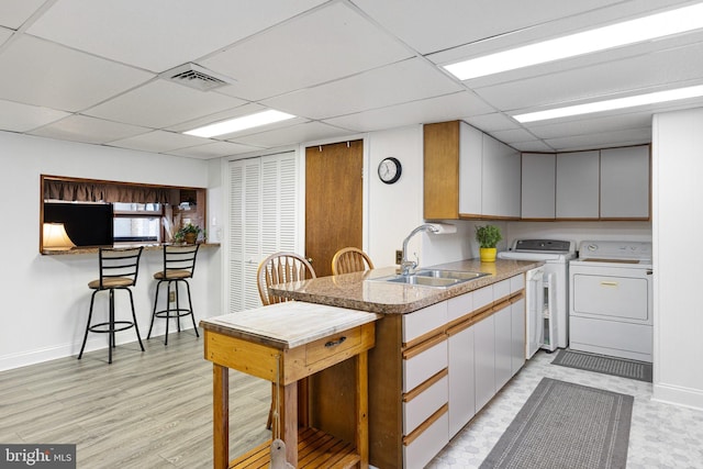 kitchen with light hardwood / wood-style flooring, a paneled ceiling, sink, and separate washer and dryer