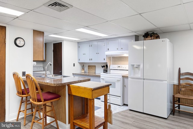 kitchen featuring white appliances, sink, a drop ceiling, kitchen peninsula, and light hardwood / wood-style floors