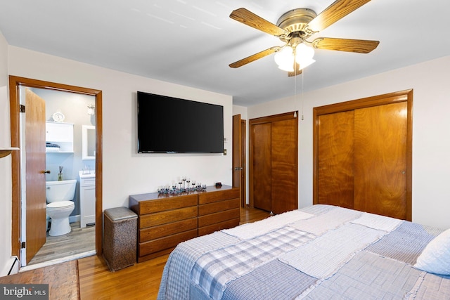 bedroom with two closets, a baseboard radiator, ceiling fan, light hardwood / wood-style floors, and ensuite bath