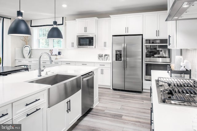 kitchen featuring exhaust hood, appliances with stainless steel finishes, decorative light fixtures, and white cabinetry