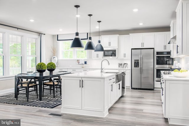 kitchen with appliances with stainless steel finishes, hanging light fixtures, a kitchen island with sink, and white cabinetry