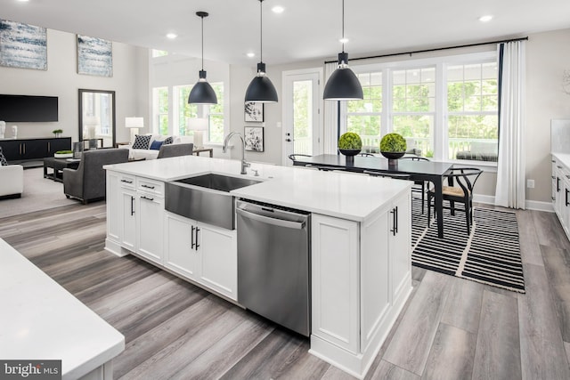 kitchen with hanging light fixtures, white cabinetry, a kitchen island with sink, stainless steel dishwasher, and sink