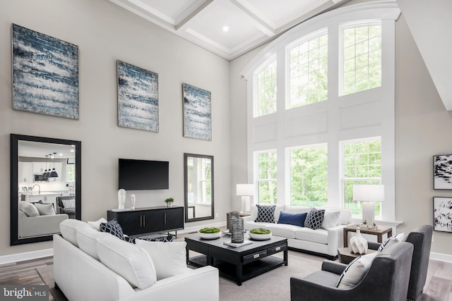 living room featuring a towering ceiling, coffered ceiling, wood-type flooring, and beam ceiling