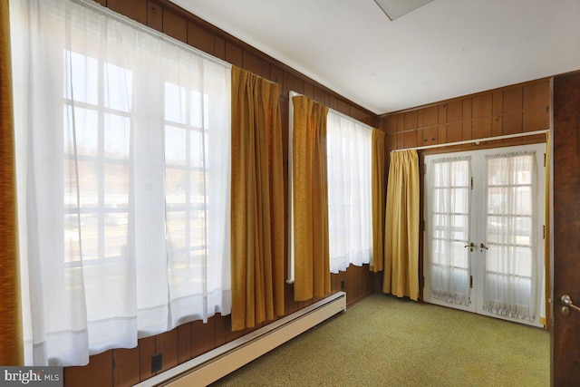 empty room featuring light colored carpet, french doors, baseboard heating, and wooden walls