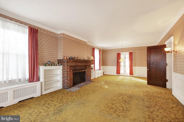 unfurnished living room featuring crown molding, radiator heating unit, a healthy amount of sunlight, and a brick fireplace