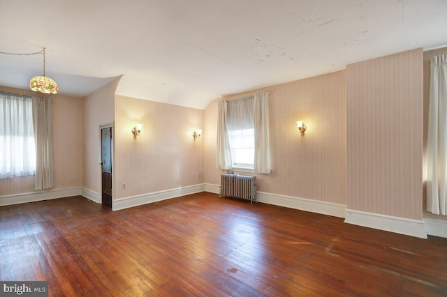 empty room with lofted ceiling, radiator heating unit, and dark hardwood / wood-style floors