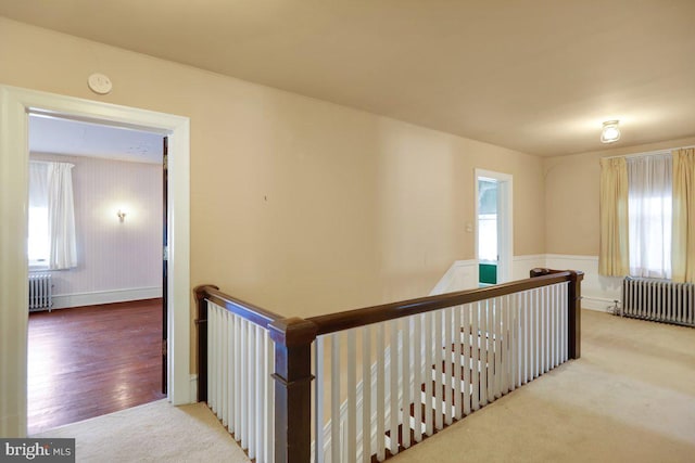 hall with light hardwood / wood-style flooring, radiator heating unit, and a healthy amount of sunlight