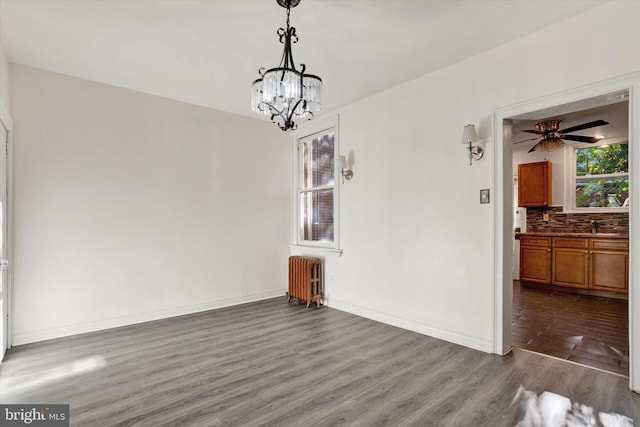 unfurnished dining area featuring ceiling fan with notable chandelier, dark hardwood / wood-style flooring, and radiator