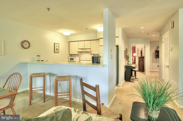 kitchen with light carpet, kitchen peninsula, white cabinets, and range