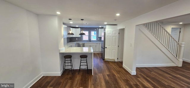 kitchen with kitchen peninsula, white cabinets, a kitchen bar, appliances with stainless steel finishes, and dark hardwood / wood-style flooring