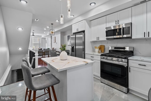 kitchen featuring a kitchen island, backsplash, light stone countertops, white cabinets, and appliances with stainless steel finishes