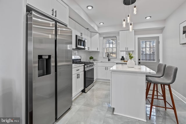 kitchen with appliances with stainless steel finishes, a kitchen bar, a center island, white cabinetry, and pendant lighting