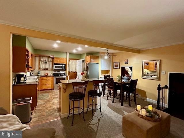 kitchen with a breakfast bar area, appliances with stainless steel finishes, ceiling fan, crown molding, and a center island