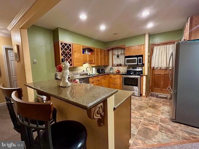 kitchen featuring kitchen peninsula, stainless steel appliances, dark stone countertops, crown molding, and a kitchen bar