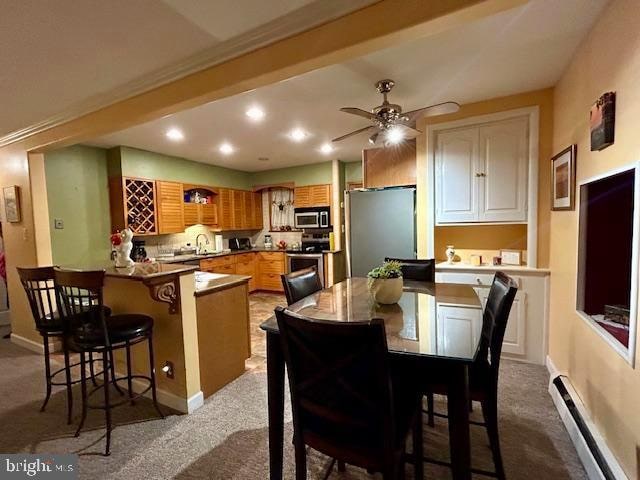 carpeted dining space featuring baseboard heating, ornamental molding, sink, and ceiling fan