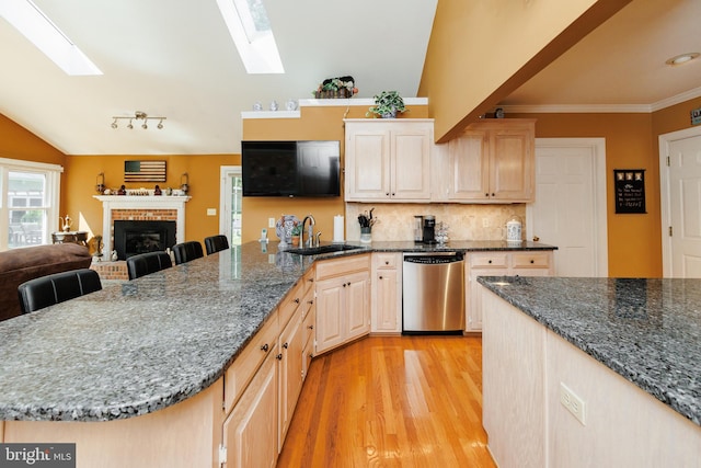 kitchen featuring vaulted ceiling with skylight, a breakfast bar, stainless steel dishwasher, and sink