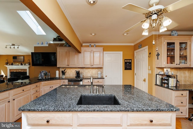 kitchen with light brown cabinetry, sink, crown molding, and dark stone counters