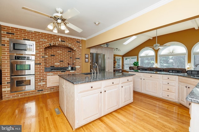 kitchen featuring an island with sink, hanging light fixtures, stainless steel appliances, dark stone countertops, and light hardwood / wood-style floors