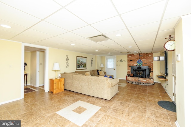 living room featuring a paneled ceiling, tile patterned floors, and a wood stove