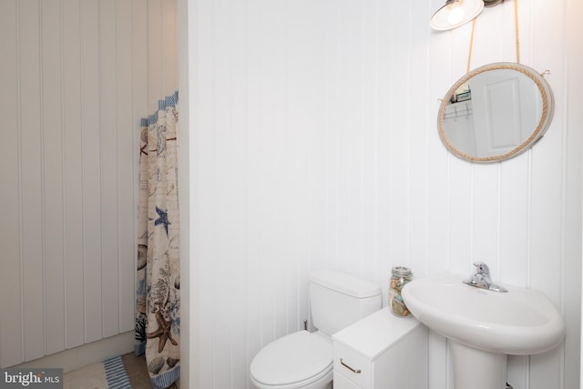 bathroom with toilet, sink, wooden walls, tile patterned floors, and a shower with shower curtain