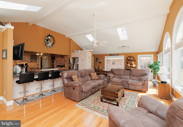 living room with beam ceiling, light wood-type flooring, a skylight, high vaulted ceiling, and ceiling fan