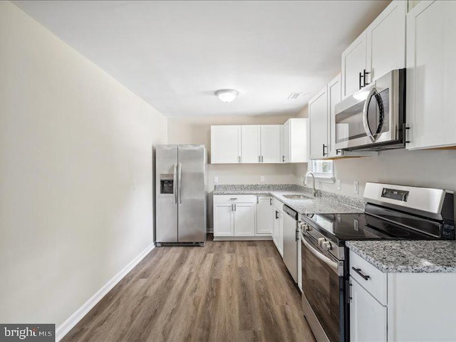 kitchen featuring stainless steel appliances, sink, light stone countertops, white cabinets, and light hardwood / wood-style floors