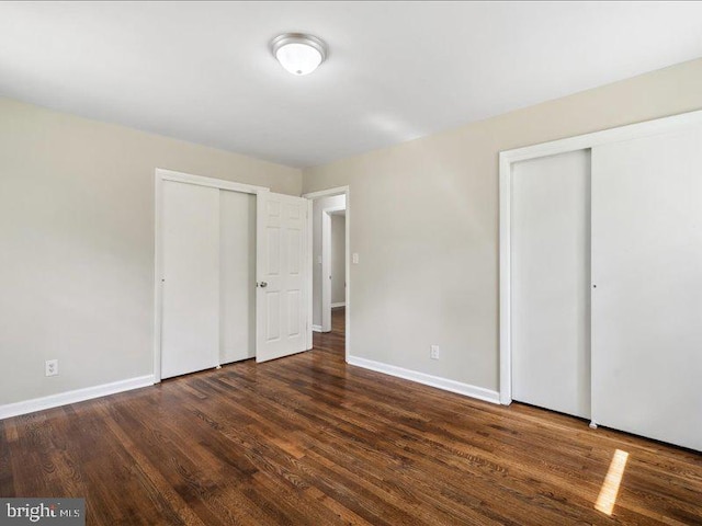 unfurnished bedroom with two closets and dark wood-type flooring