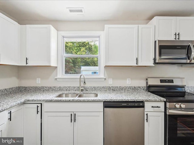 kitchen with light stone counters, appliances with stainless steel finishes, sink, and white cabinets