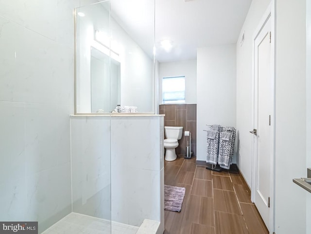 bathroom featuring toilet, a shower, and tile walls