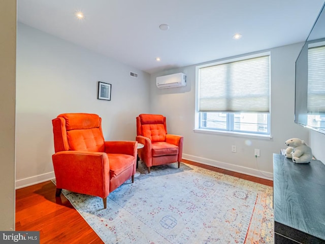 sitting room featuring an AC wall unit and wood-type flooring