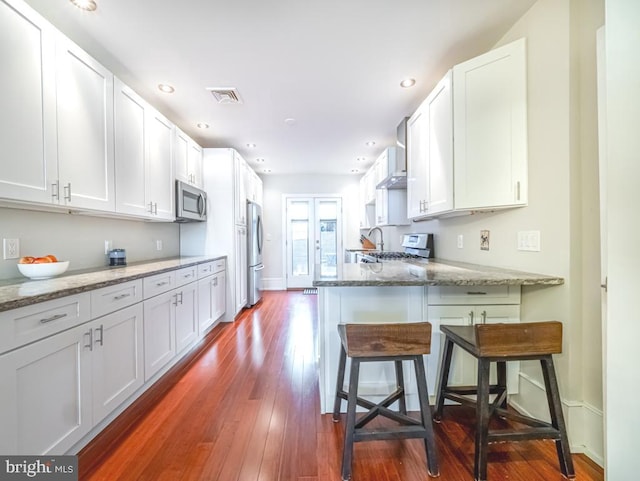 kitchen featuring white cabinetry, stainless steel appliances, stone counters, and a kitchen bar