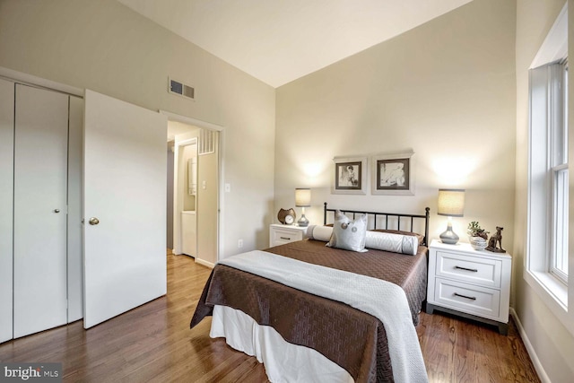 bedroom featuring high vaulted ceiling, wood-type flooring, and a closet