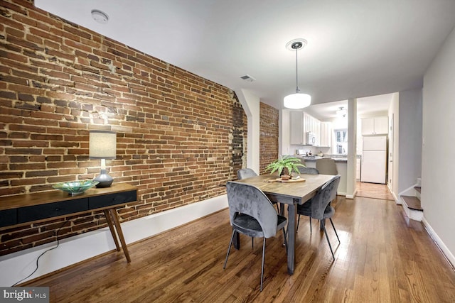 dining area with brick wall and light hardwood / wood-style floors