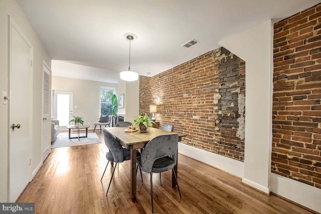 dining space featuring brick wall and wood-type flooring