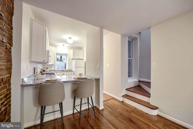 kitchen featuring white cabinetry, white fridge, hardwood / wood-style flooring, and light stone countertops