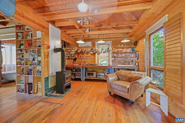 living area featuring wood walls, an AC wall unit, a wood stove, hardwood / wood-style floors, and beam ceiling