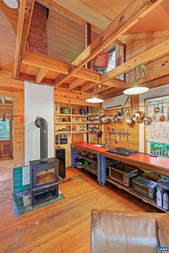 living room with vaulted ceiling with beams, a wall unit AC, wood-type flooring, a wood stove, and wood walls