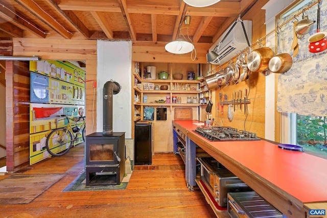 kitchen with stainless steel gas stovetop, light wood-type flooring, a wall mounted air conditioner, a wood stove, and decorative light fixtures