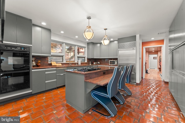 kitchen with a kitchen island, built in appliances, backsplash, a kitchen bar, and decorative light fixtures