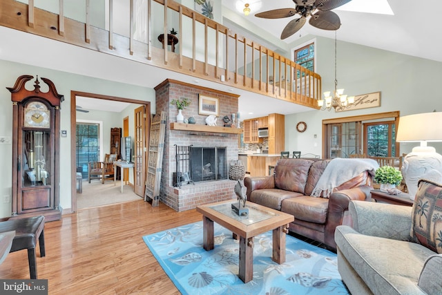 living room featuring a wealth of natural light, ceiling fan with notable chandelier, a brick fireplace, and wood finished floors